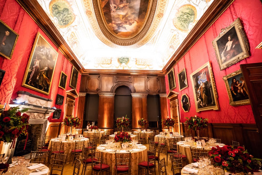 Dinner set up on round tables in the King's Drawing Room with red florals and uplighting.