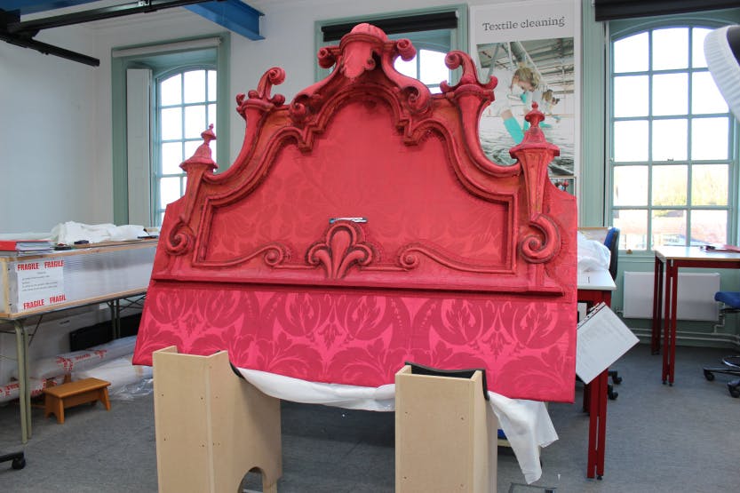 Conservation of the 18th Century headboard from Queen Caroline's State Bed. Showing the red silk damask headboard in the Conservation Studio during its conservation treatment.