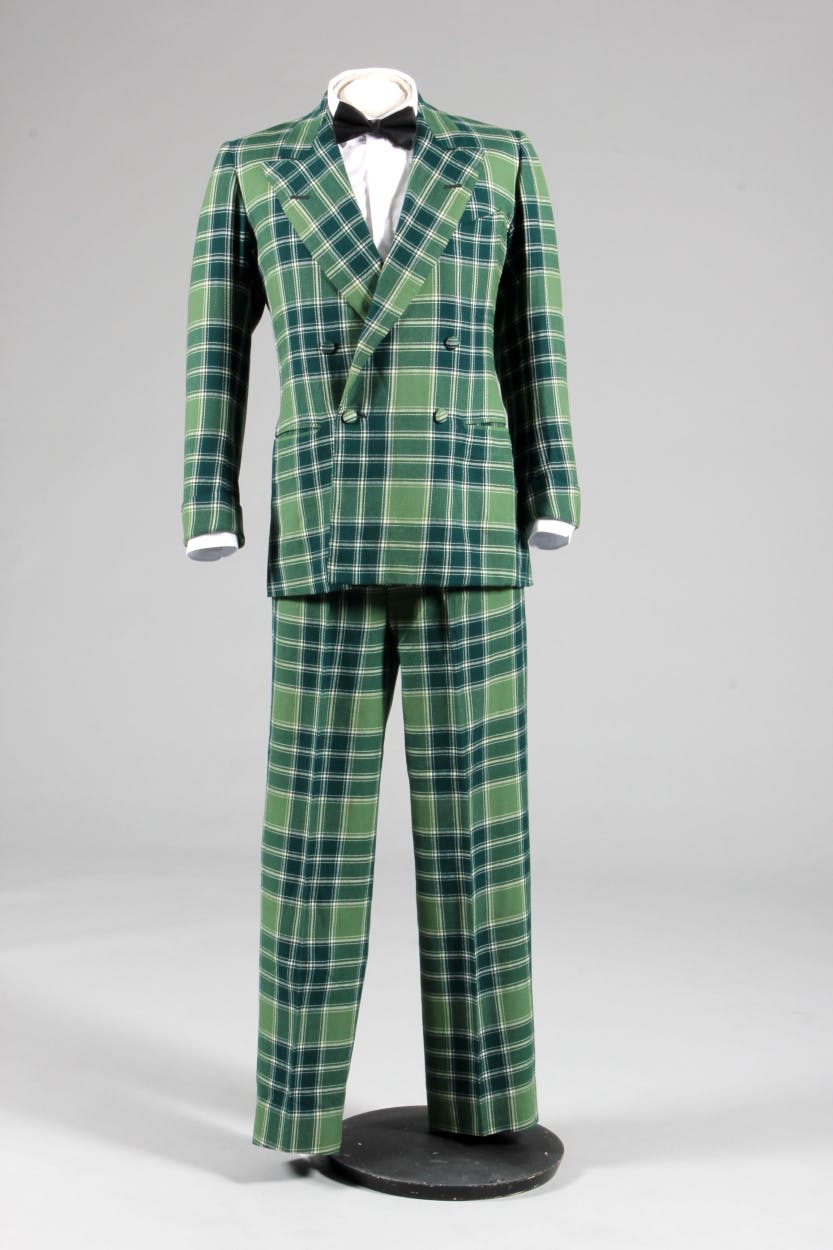 Lord of the Isles woven wool tartan suit worn by the Duke of Windsor. Elements of the suit are made by different tailors. Jacket by Scholte (jacket), trousers tailor made in New York. The green tartan suit is displayed on a mannequin and photographed against a grey background.