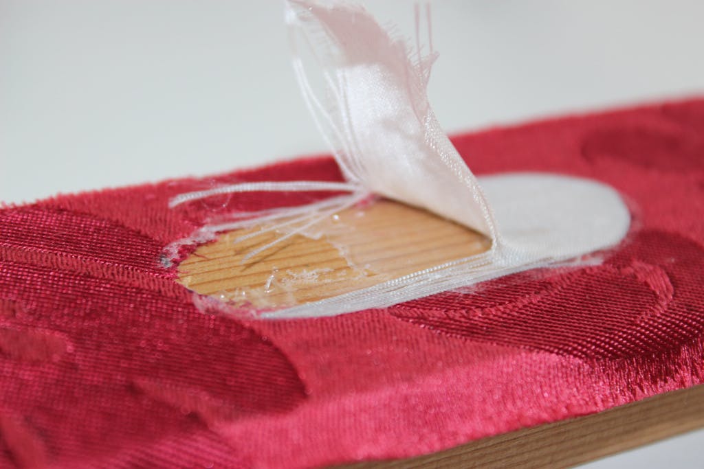 Conservation of Queen Caroline's State Bed. Showing a close up of a trial to remove a patch on the red damask using a heated spatula