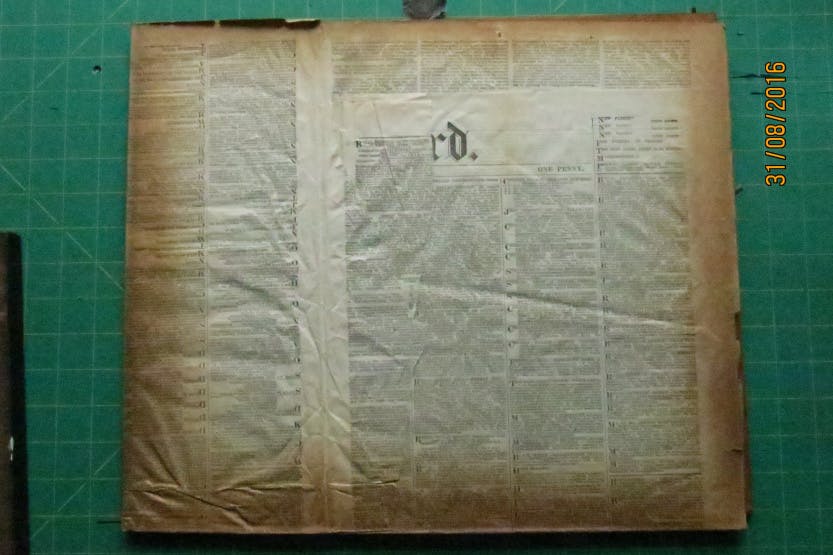 An old newspaper found as a lining after the removal of a print from a wooden frame. Shows the mark left by the oak frame, yellowing the paper.