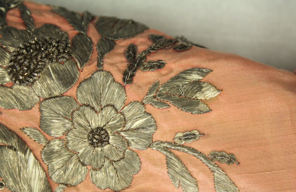Close up detail of the metal embroidery on a pink watered silk jacket worn by Queen Victoria, showing tarnishing.