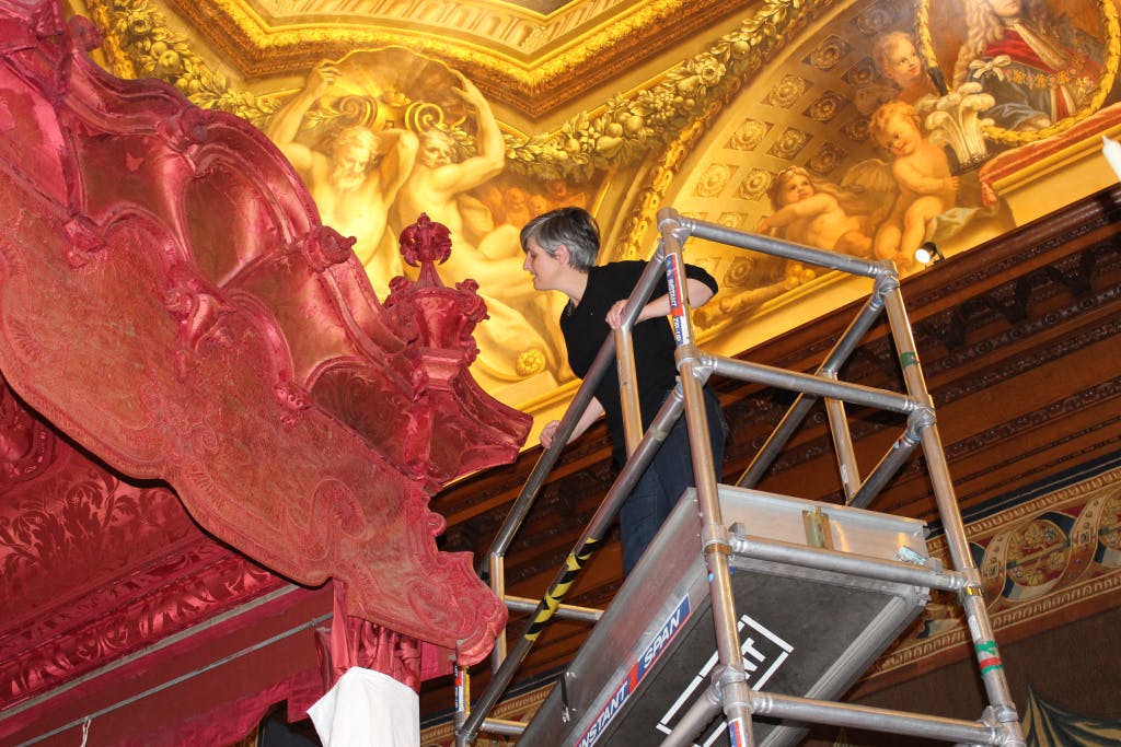 Conservation of Queen Caroline's State Bed. Showing Rebecca Bissonnet (Conservation Supervisor) on scaffolding examining the cornices and corbels before de-installation