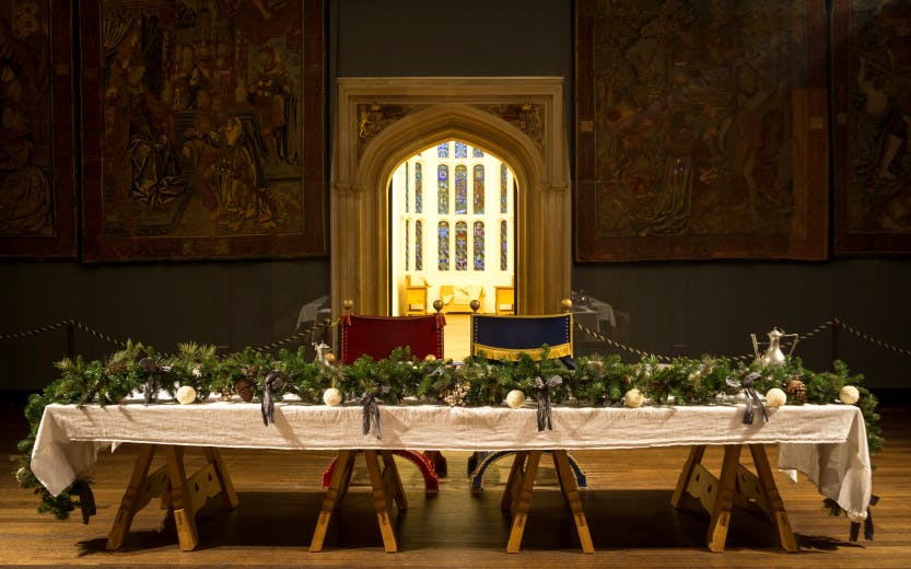 Christmas holly and foliage on the main table in the Great Hall at Hampton Court Palace, surrounded by Tudor tapestries.