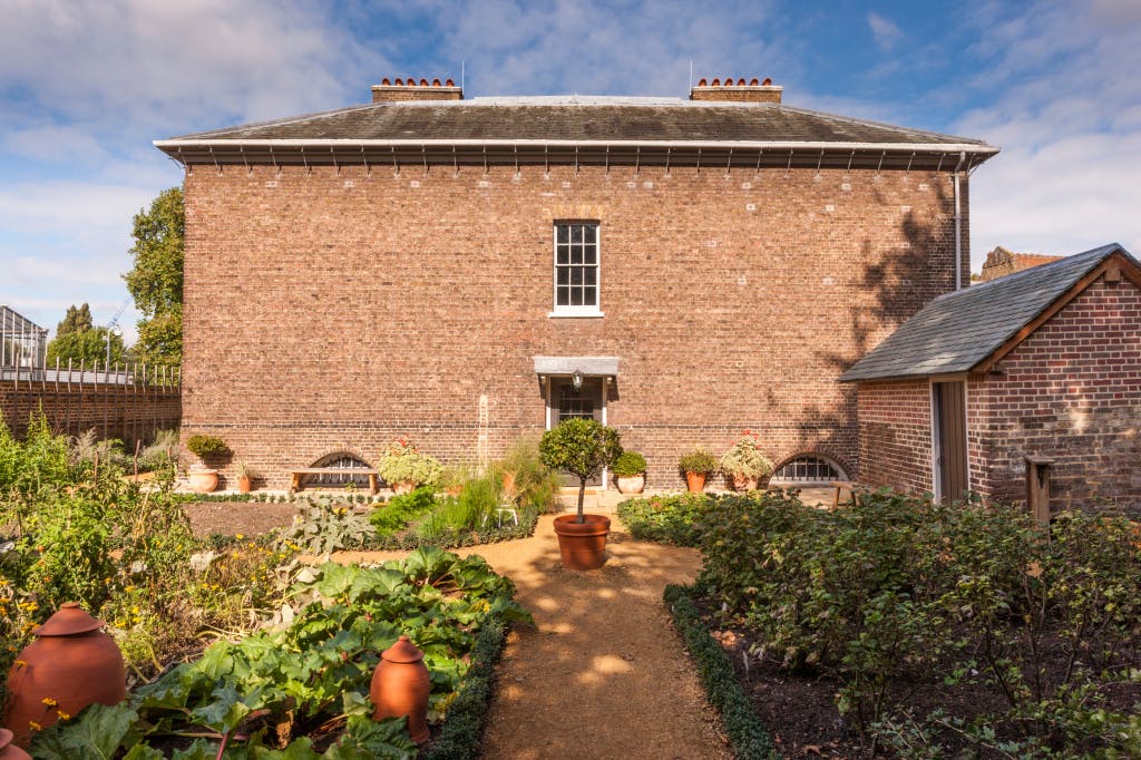 The Royal Kitchens and the Kitchen Garden following restoration in 2013. Looking from the Kitchen Garden to the entrance to the Royal Kitchens. A bay tree in a terracotta pot stands on the garden path and vegetables including rhubarb are growing in beds on either side of the pathway.