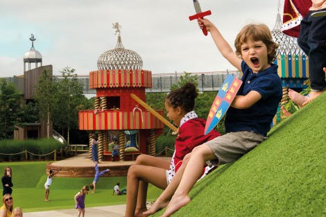 A boy holds up a toy sword and shouts as children play in the background at the Magic Garden at Hampton Court Palace