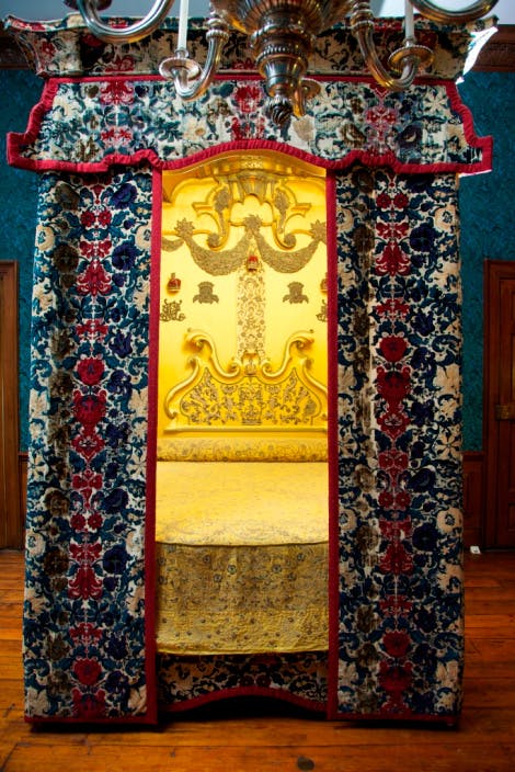 The Queen’s Bedroom, looking north. Showing the 'Mary of Modena' bed, traditionally regarded as the bed made for King James II and Mary of Modena. It is also known as the 'warming pan bed' and is associated with the birth of Prince James Francis Edward Stuart (the 'Old Pretender') at St James's Palace in 1688. The 19th century head cloth and head board is in applied embroidered decoration with the crowns and cyphers of James and Mary. The bed stock is in early yellow silk embroidery dating from around 1720 (later reconfigured). The counterpane is high-quality floral embroidery with silver-gilt thread dating from around 1650-60.