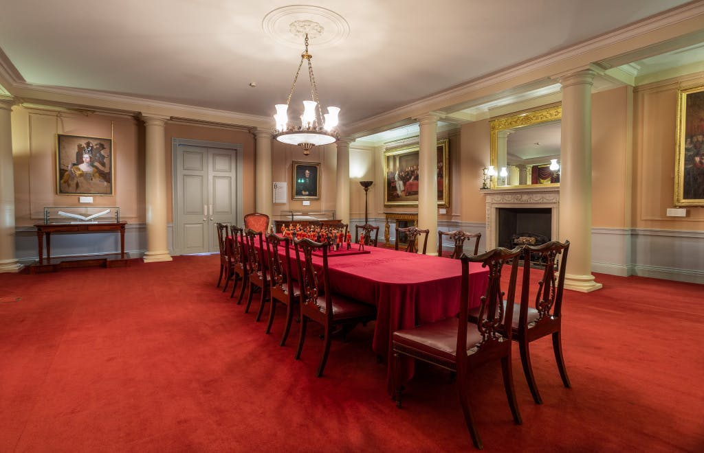 Victorian period furniture in a red room. There is a bright red carpet on the floor and a large dining table in the middle of the room