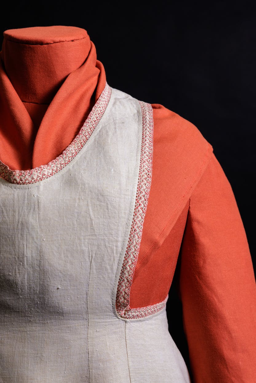 Close up view of white cotton apron with red trim that belonged to Elizabeth Anne Thielcke. Shot in front of a black background.