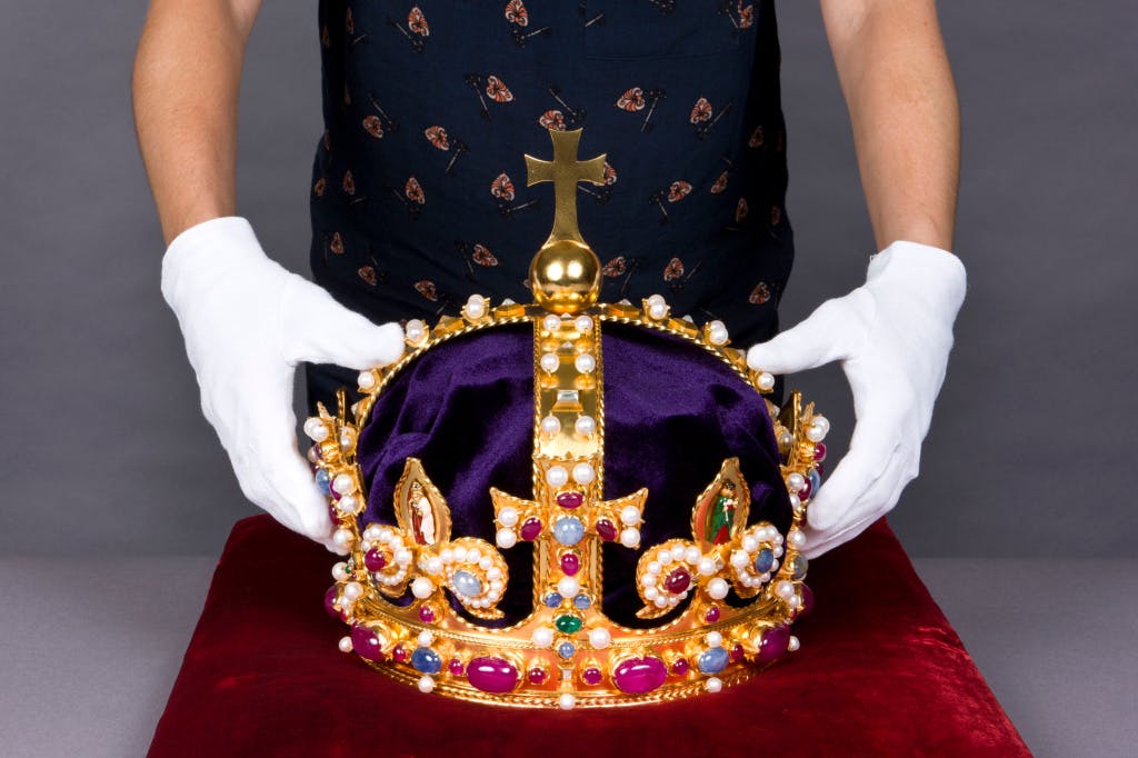 A conservator's white-gloved hands holding a recreation of the jewelled State Crown worn by King Henry VIII.