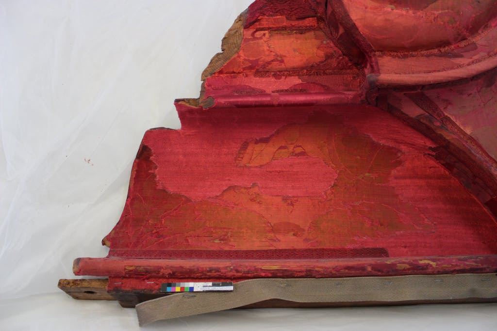 Conservation of Queen Caroline's State Bed. Showing  close up of disfiguring patches on the red damask.