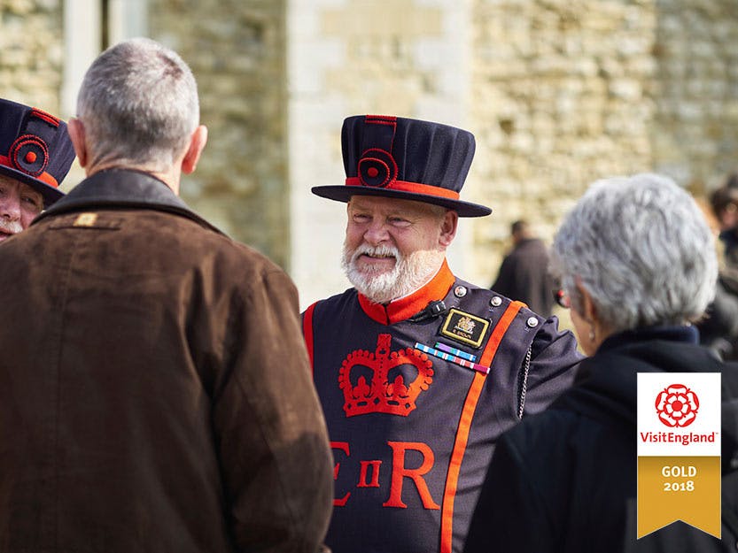 A male staff member from the Yeoman Body is shown in their full uniform/regalia speaking with a male and female visitor.