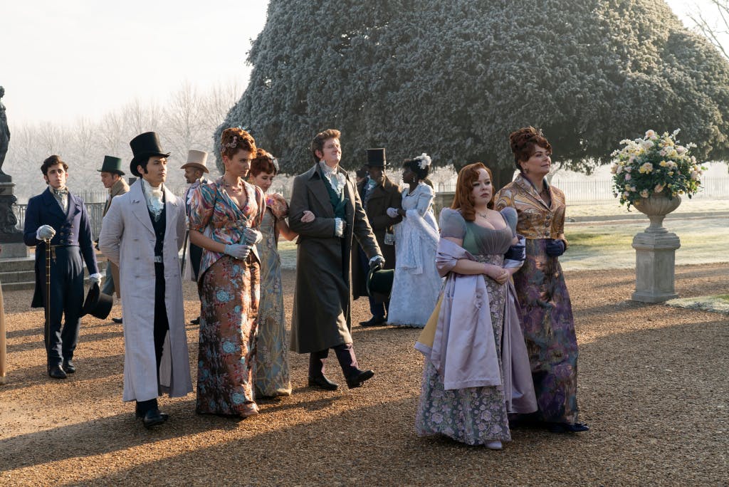 A group of people dressed in regency costumes in the gardens at Hampton Court Palace.