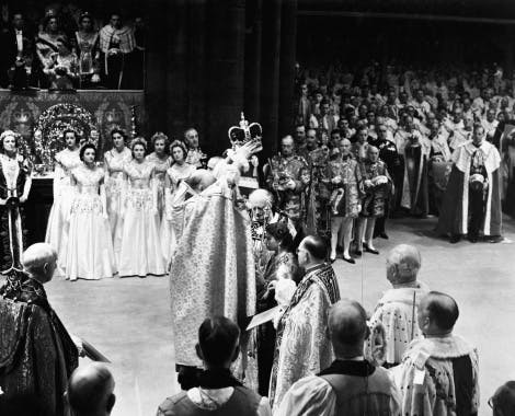 Man crowns the queen at her coronation in Westminster Abbey surrounded by spectators