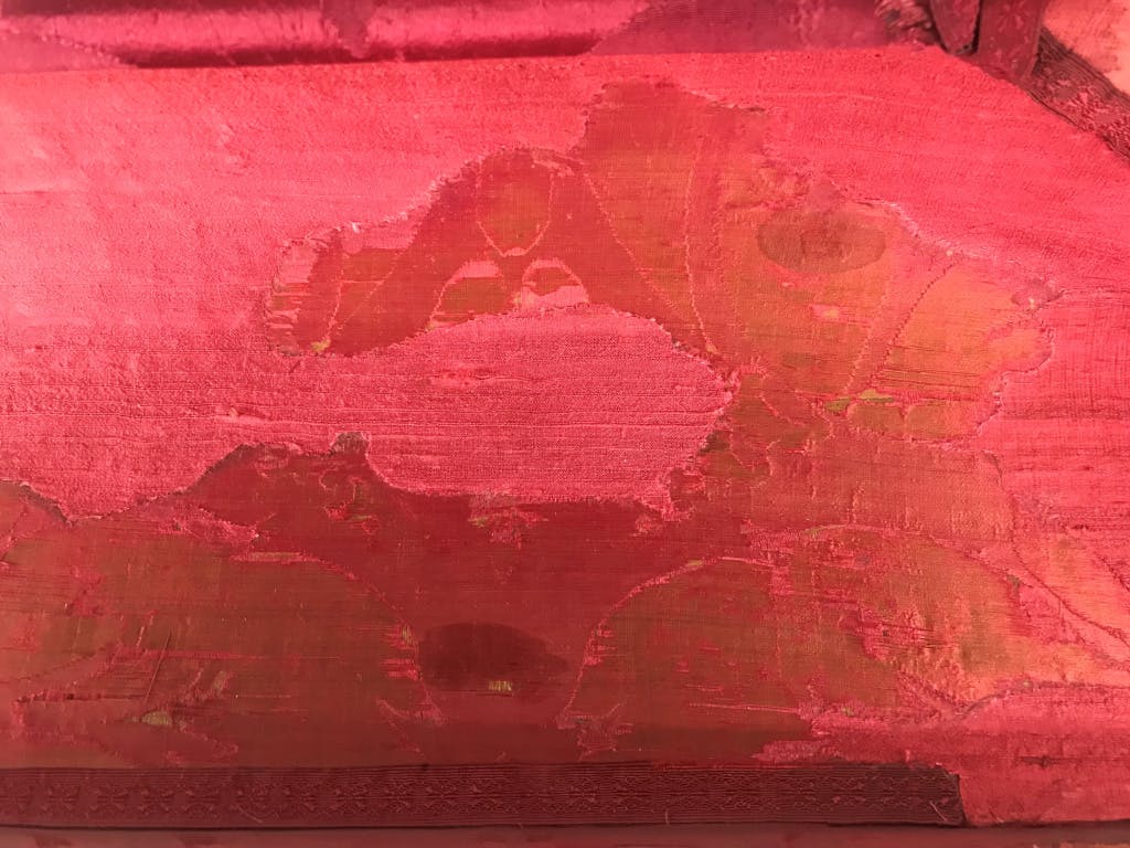 Conservation of Queen Caroline's State Bed. Showing a close up of patches on the red damask.