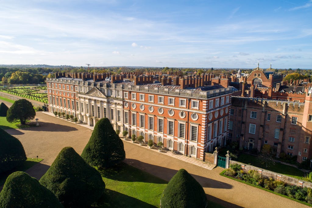 Aerial view over Hampton Court Palace and gardens looking south-west down towards the East Front, autumn 2023. Some of the yew trees in the Great Fountain Garden are seen in the foreground.