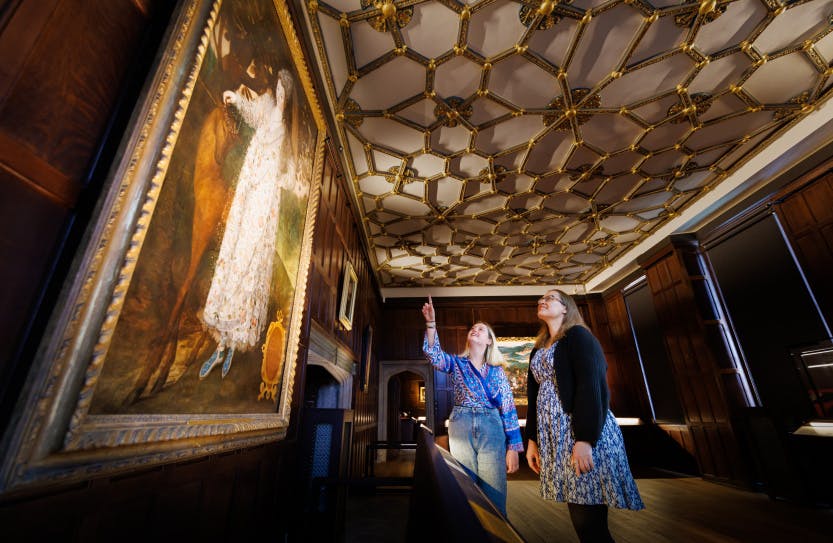 Two staff members pointing at a portrait of an 'Unknown Lady' painted by Marcus Gheeraerts the Younger in the HCP Wolsey Room Tudor World exhibition space.