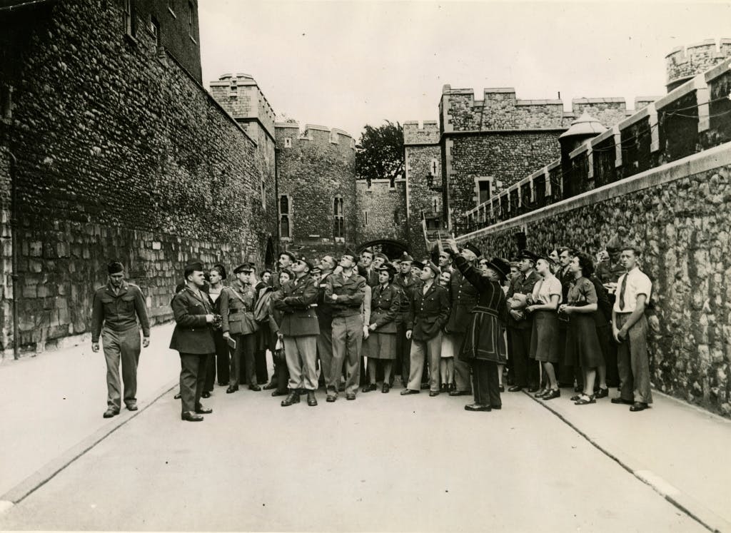 Yeoman Warder Sprake in Water Lane, with group of servicemen and women. Sprake is pointing to the Council Chamber in the King's House where Guy Fawkes was examined. Image dated 1945.