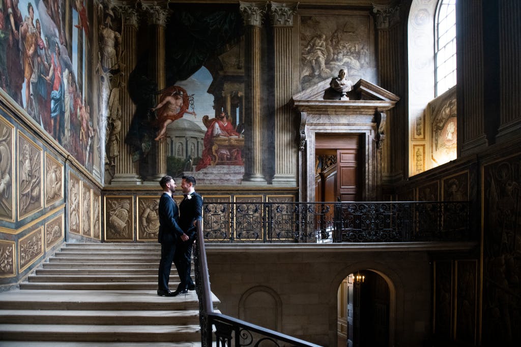 Wedding photos from Will and Jonny's Little Banqueting House Wedding Ceremony. The couple standing in the Kings Staircase, facing each other with the backdrop of the top of the stair and door to the Kind's route.
