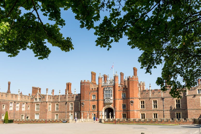 Tudor West Gate of Hampton Court Palace under a blue sky. Visitors can be seen in the foreground