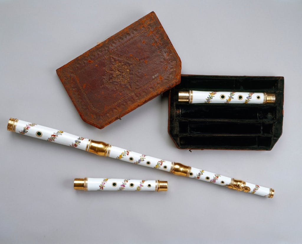 A small white flute and case displayed on a grey background