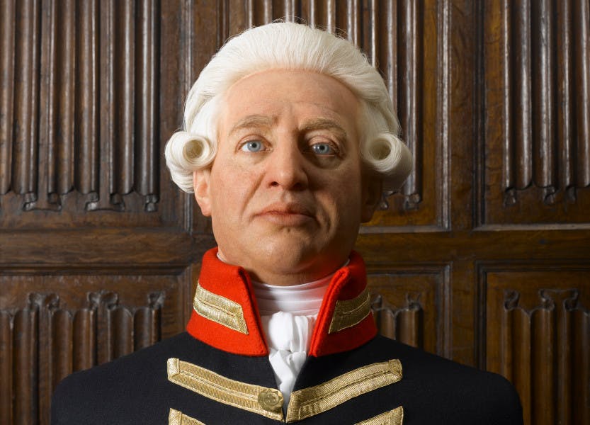 A wax bust depicting King George III in military uniform. The King wears a white period-style wig and is placed in front of a brown, linenfold panelled wall