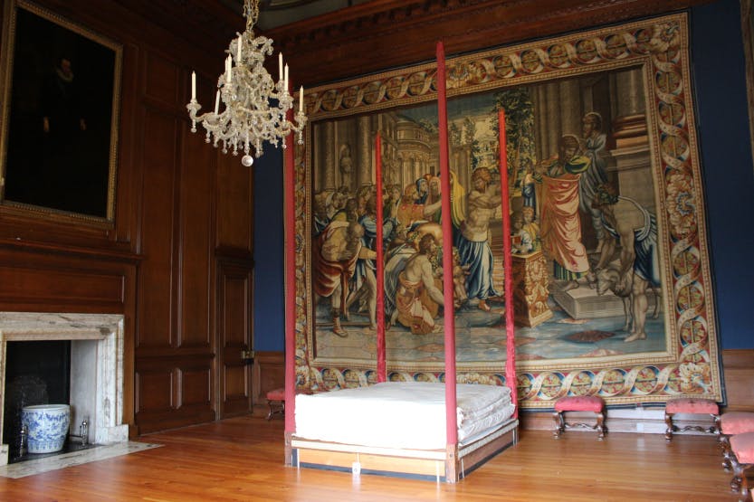 A group of people moving a large red bed frame in a room lined with tapestries