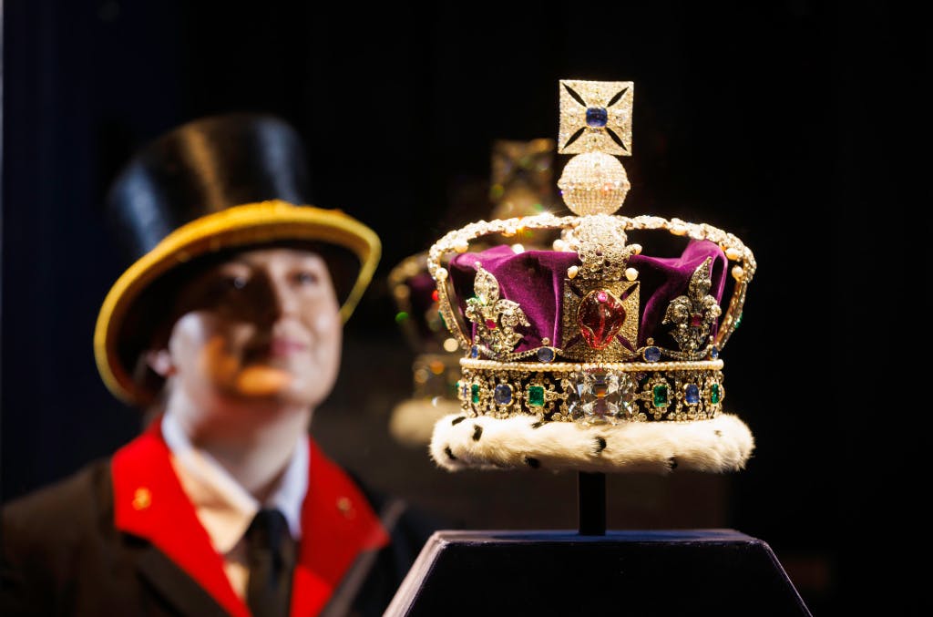 A close view of Hazel Dincer (Jewel House Warder) in uniform (face blurred) looking at the Imperial State Crown. (Photographed against a black background.)