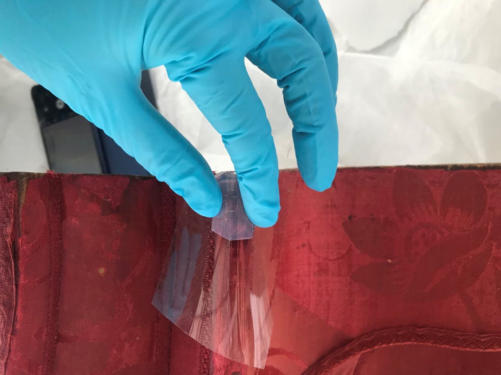 Conservation of Queen Caroline's State Bed. Showing a Conservator's hand Removing a patch on the cornice using a gel.