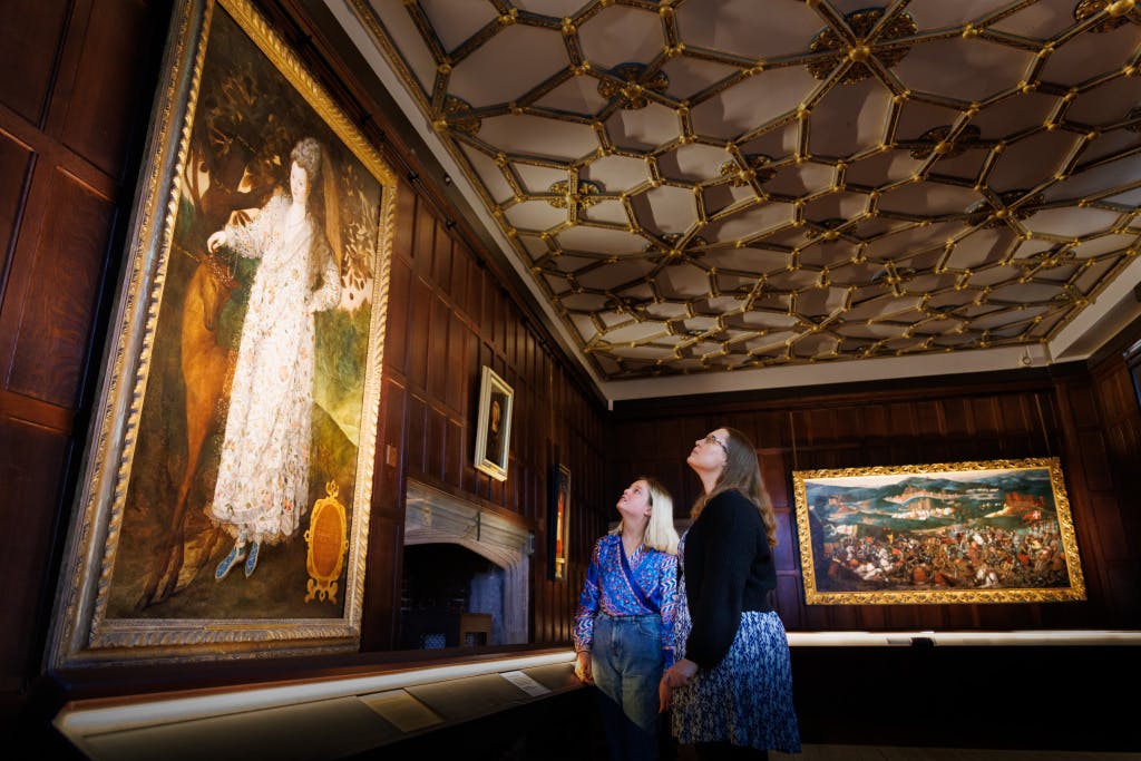 Two staff members admiring a portrait of an 'Unknown Lady' painted by Marcus Gheeraerts the Younger in the HCP Wolsey Room Tudor World exhibition space.