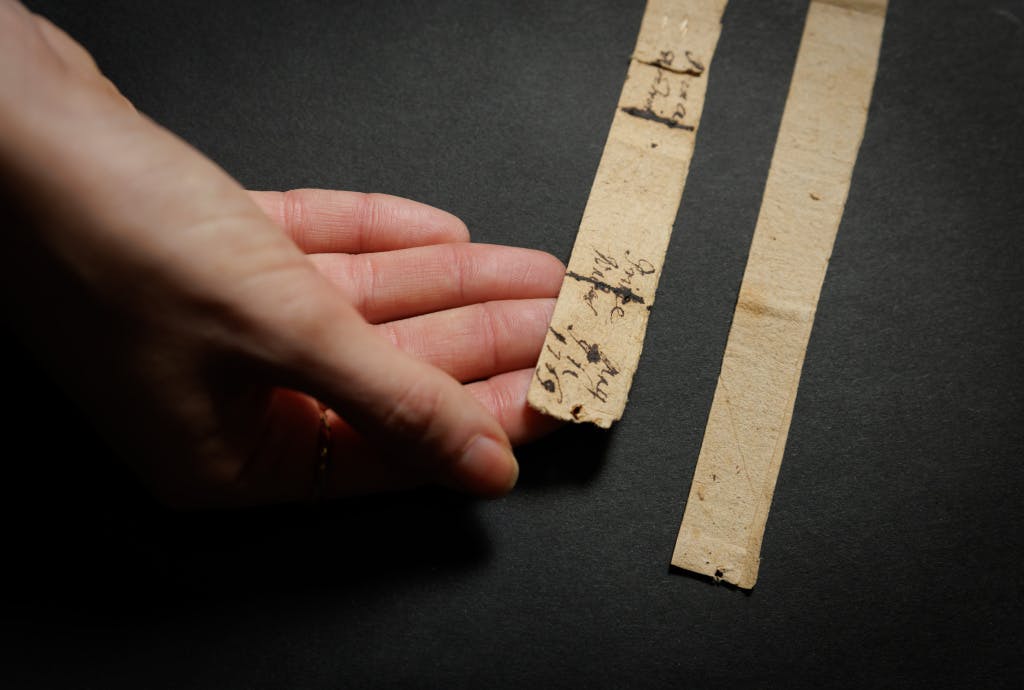 Close up of a conservator's hands laying out a paper tape measure used to measure the heights of the children of King George III and Queen Charlotte. Photographed against a black background.