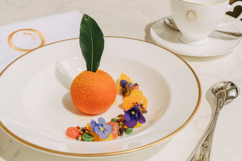 Plate of food, showing a dessert decorated to look like an orange.